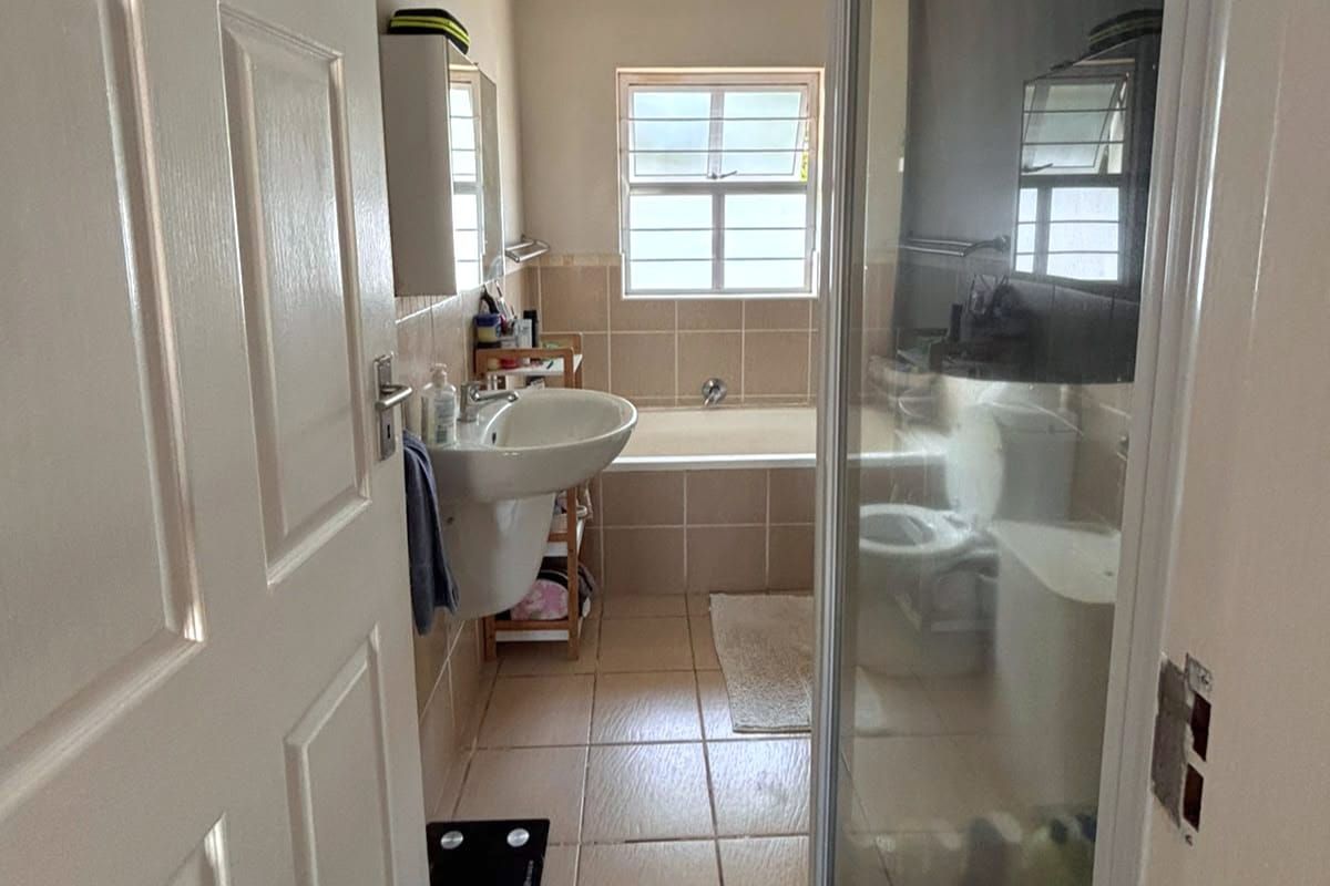A functional bathroom featuring a pedestal basin, a built-in bathtub, and a separate shower enclosure with tiled finishes throughout.