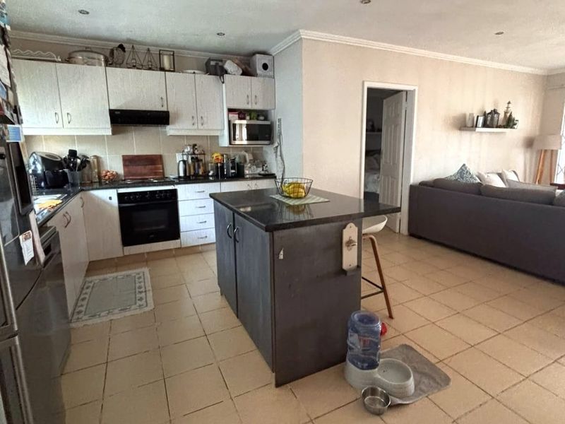 Open plan kitchen featuring a central island, built-in oven, and tiled flooring, seamlessly connecting to the adjacent living area.
