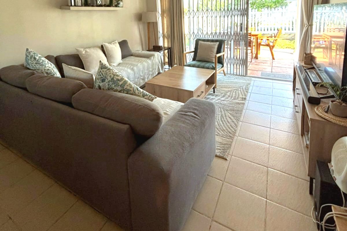 A comfortable living room featuring tiled flooring and a sliding glass door with a security gate, providing direct access to the outdoor patio area.