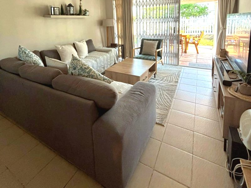 A comfortable living room featuring tiled flooring and a sliding glass door with a security gate, providing direct access to the outdoor patio area.