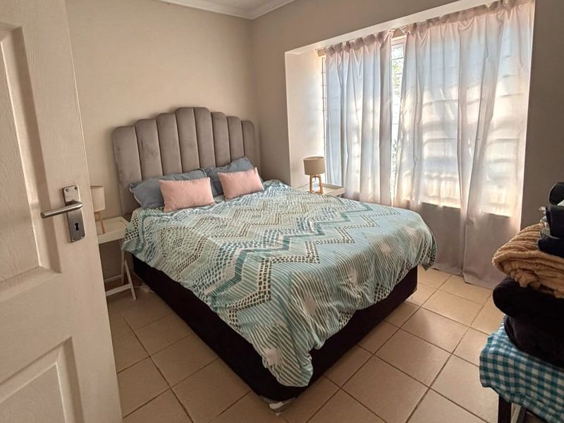 A functional bedroom featuring tiled flooring, coved ceiling details, and a large window with security bars, providing natural light.