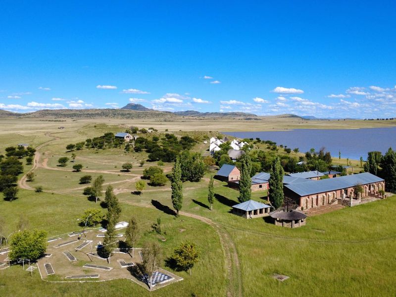 Aerial view of a sprawling farm estate featuring multiple brick buildings, a miniature golf course, and extensive grounds overlooking a large lake.