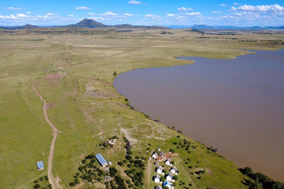 An aerial view of the farm property featuring multiple buildings situated along the edge of a large dam with expansive surrounding landscape.