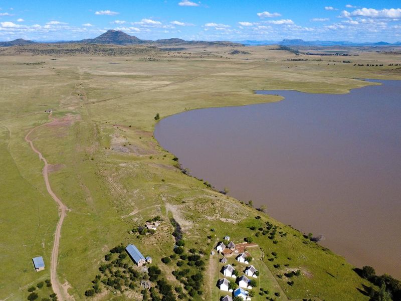 An aerial view of the farm property featuring multiple buildings situated along the edge of a large dam with expansive surrounding landscape.