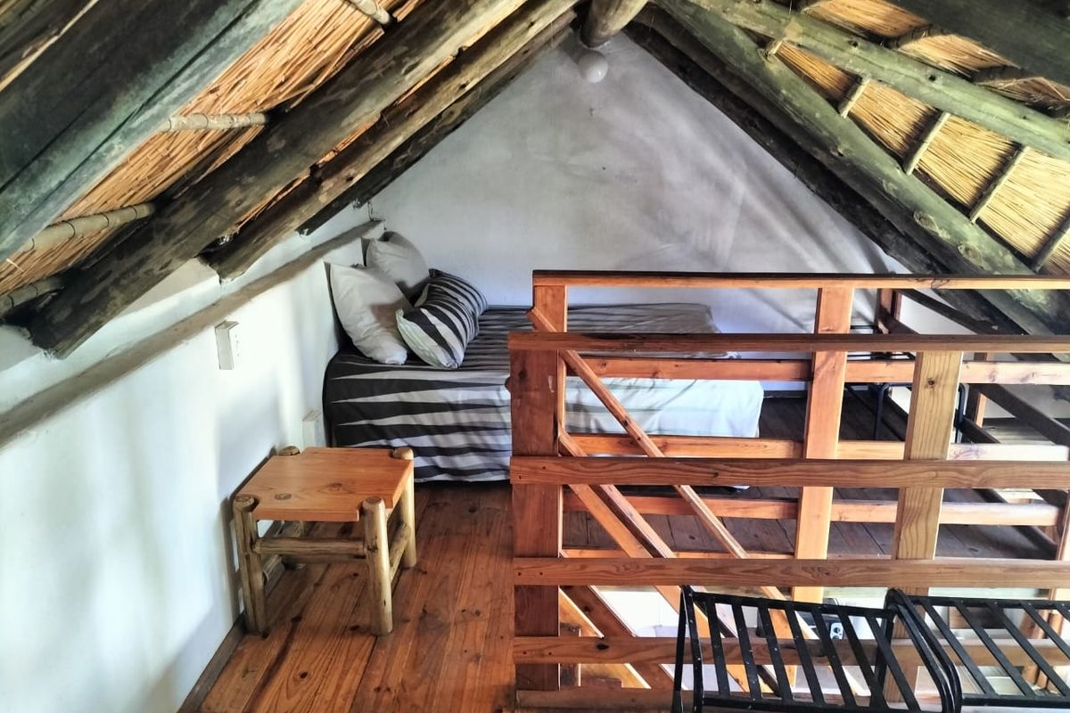 A rustic loft bedroom featuring exposed timber rafters, a traditional thatched roof, and wooden flooring with a protective timber balustrade.