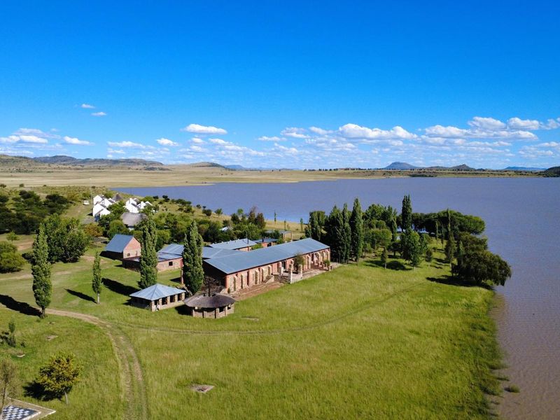 Aerial view of a rural farm property featuring multiple brick buildings with metal roofs, a thatched gazebo, and extensive waterfront access.