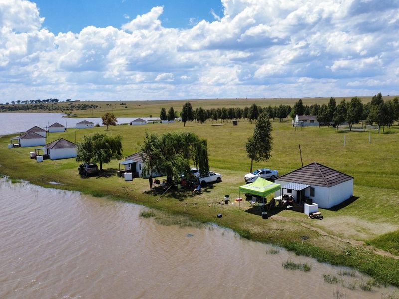Aerial view of a waterfront farm property featuring multiple detached residential units situated along the shoreline with expansive surrounding grassland.