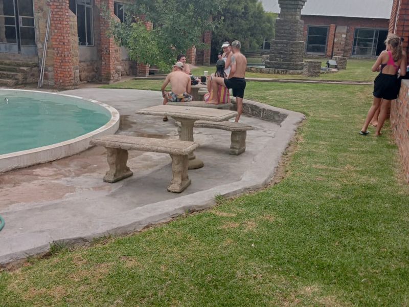 Outdoor pool area featuring exposed brick farm-style buildings, a concrete patio, and a stone fountain set within a landscaped garden.