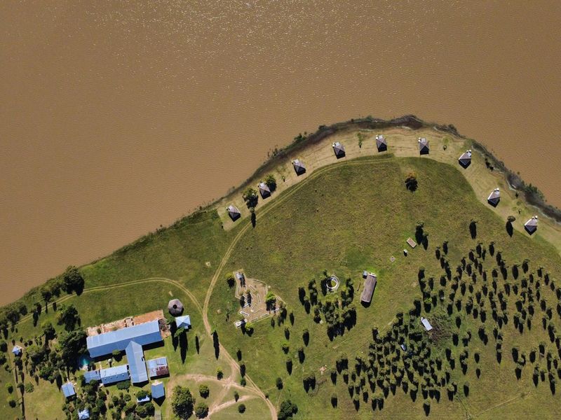 Aerial view of a waterfront farm property featuring multiple outbuildings, expansive green grounds, and direct access to the riverbank.
