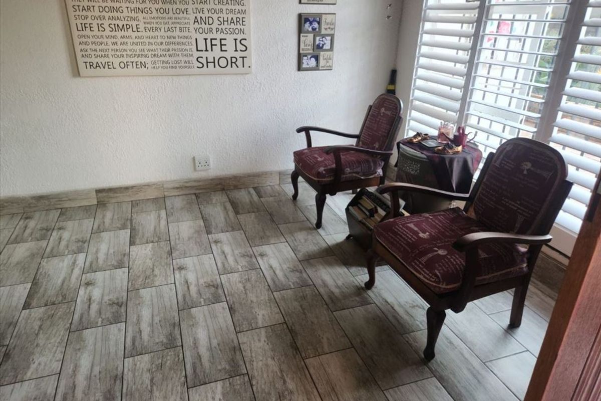 A bright living area featuring modern wood-look ceramic floor tiles and white plantation shutters, providing a clean and neutral foundation for the space.