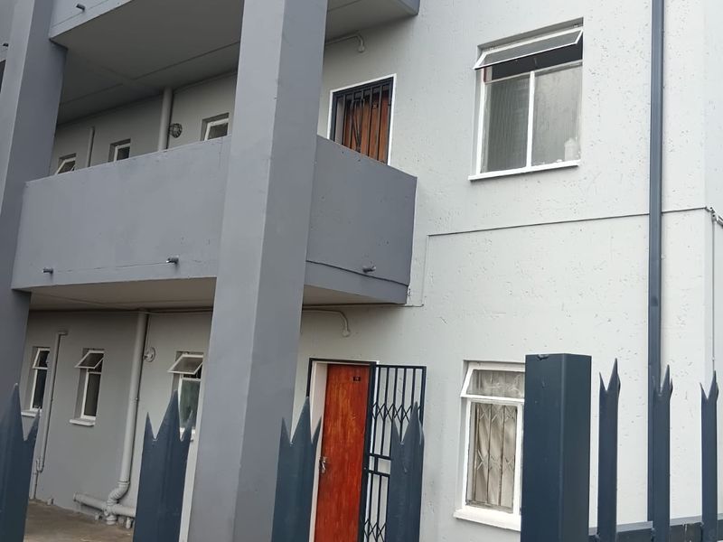 Exterior view of a multi-story flat building featuring balconies, security gates, and perimeter fencing.