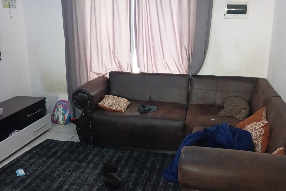 A living room area featuring tiled flooring and a wall-mounted electrical distribution board, with visible wall staining near the window curtains.