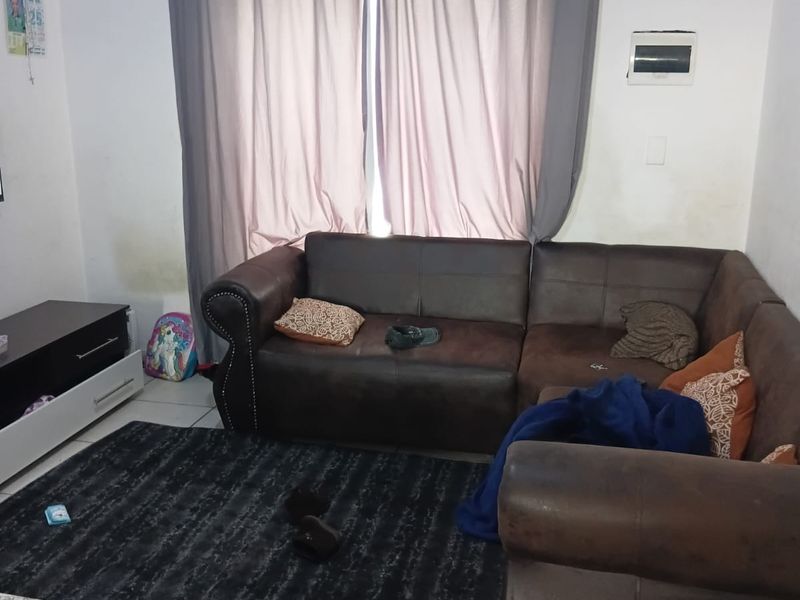 A living room area featuring tiled flooring and a wall-mounted electrical distribution board, with visible wall staining near the window curtains.