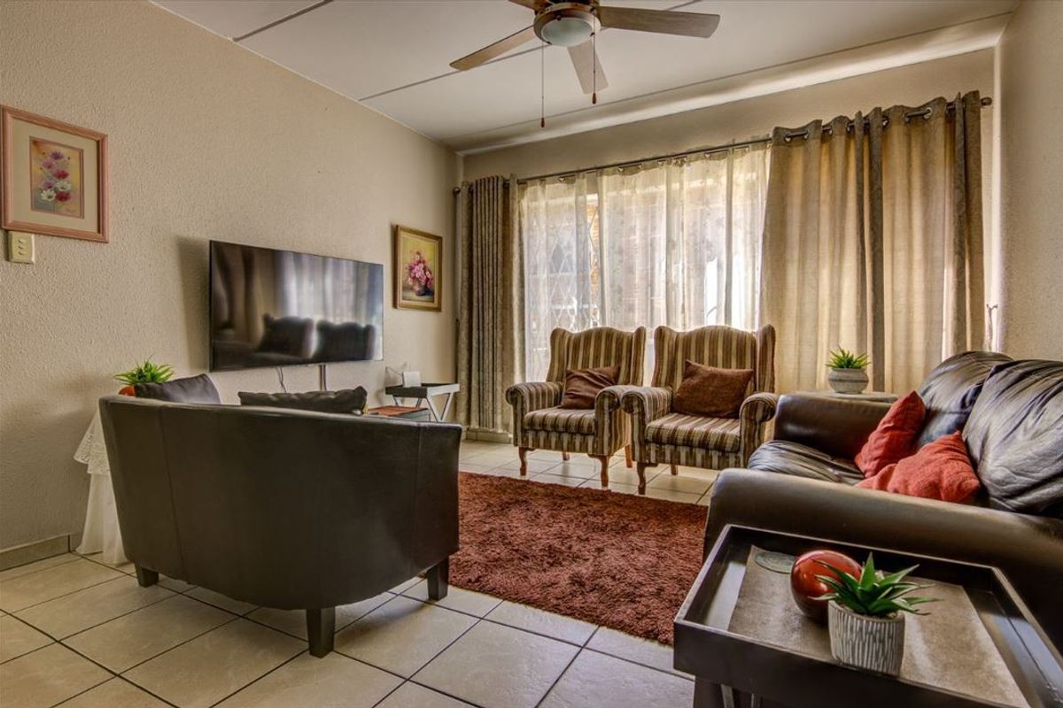 A comfortable living room featuring tiled flooring, a ceiling fan, and large windows with curtain tracks, providing a functional and well-lit space.