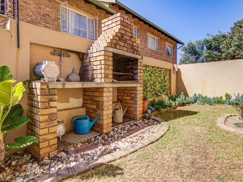 Rear garden area featuring a built-in brick braai, established garden beds, and a perimeter wall, providing a functional outdoor entertainment space.