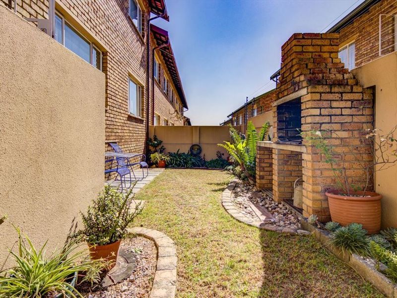 A private rear garden featuring a built-in brick braai, paved garden borders, and secure boundary walls with electric fencing.