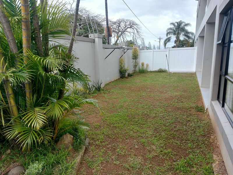 A private rear garden area featuring a lawn, perimeter wall with electric fencing, and direct access to the apartment interior via sliding glass doors.