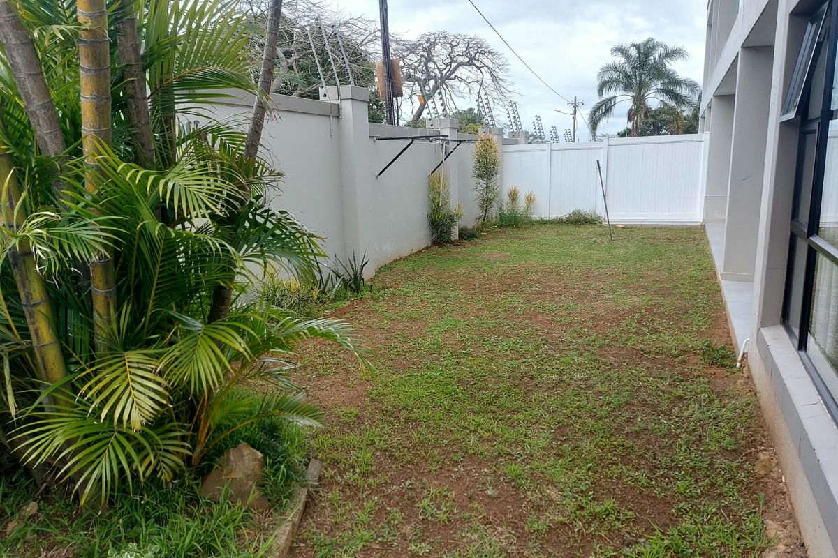 A private rear garden area featuring a lawn, perimeter wall with electric fencing, and direct access to the apartment interior via sliding glass doors.