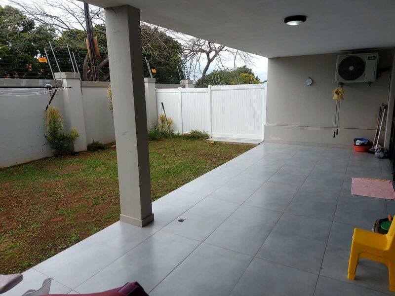 A covered patio area featuring tiled flooring, a support column, and direct access to a private garden enclosed by a perimeter wall.
