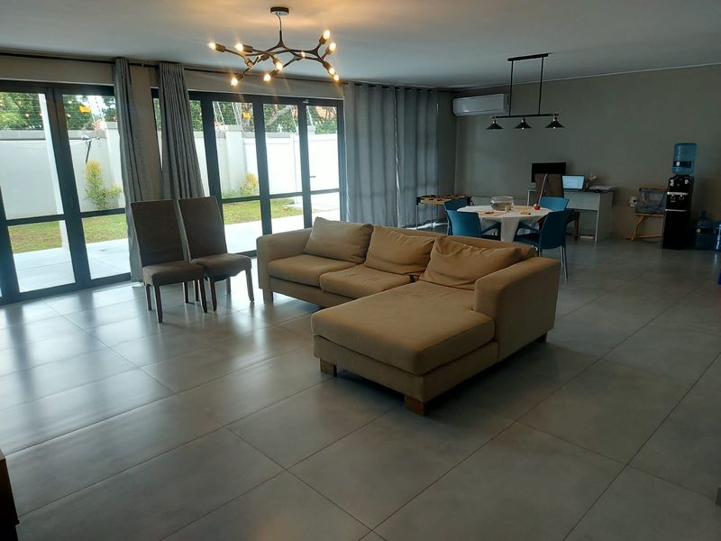 Spacious open-plan living area featuring large format floor tiles, modern lighting, and expansive aluminium sliding doors providing seamless access to the outdoor garden space.