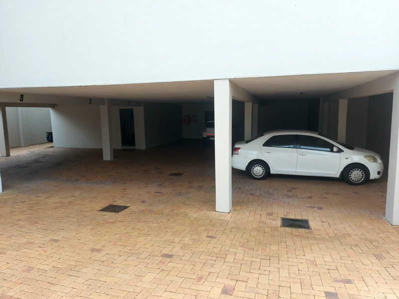 A covered parking area featuring paved flooring and concrete support pillars, providing designated parking bays for residents.