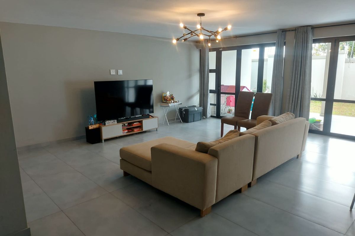 Spacious living room featuring large format floor tiles, modern lighting, and expansive glass sliding doors providing seamless access to the outdoor area.