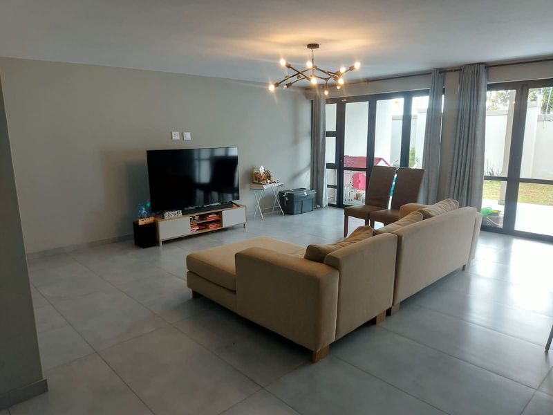 Spacious living room featuring large format floor tiles, modern lighting, and expansive glass sliding doors providing seamless access to the outdoor area.