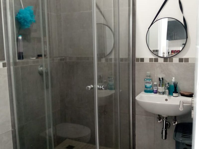 A functional bathroom featuring a glass shower enclosure, wall-mounted basin, and tiled finishes throughout.