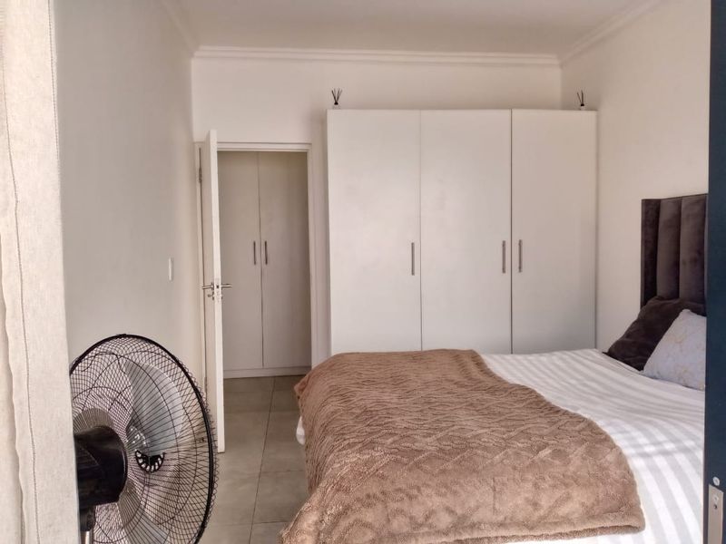 A well-maintained bedroom featuring neutral tiled flooring, built-in cupboards, and decorative ceiling cornicing.
