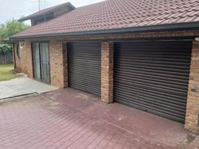 Exterior view of a double garage featuring brick construction, roller doors, and an adjacent paved area with a sliding door entrance.