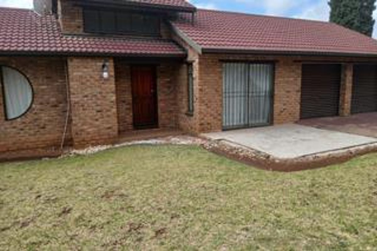 Rear view of a brick house featuring a tiled roof, concrete patio area, and double garage access with security bars on windows.