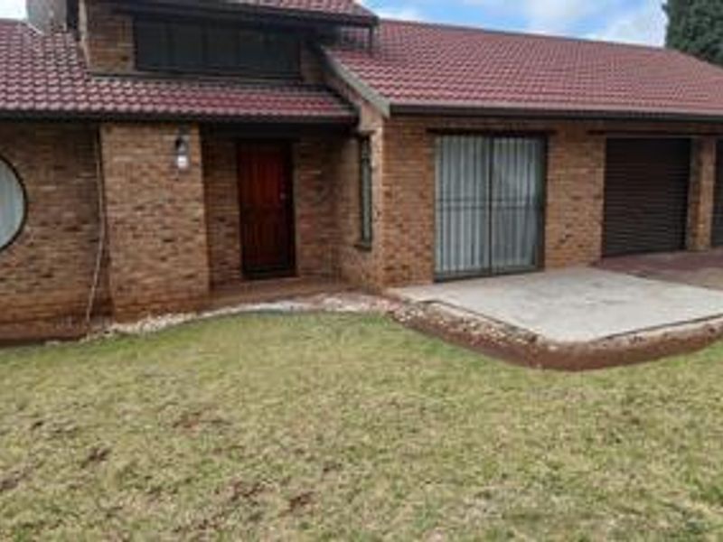 Rear view of a brick house featuring a tiled roof, concrete patio area, and double garage access with security bars on windows.