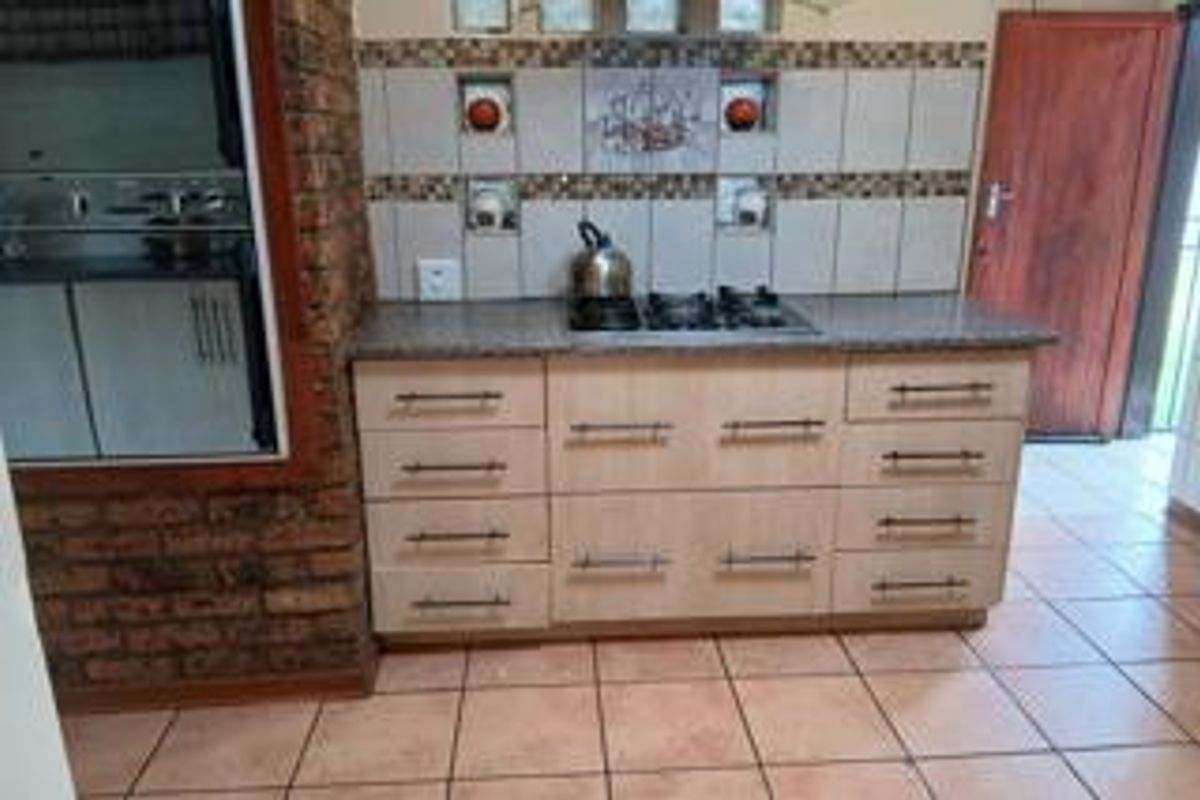 A functional kitchen area featuring light wood cabinetry, a gas hob, granite countertops, and a decorative tiled backsplash with exposed brick accents.