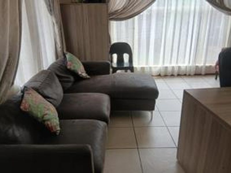 A living room area featuring tiled flooring and large windows with curtains.