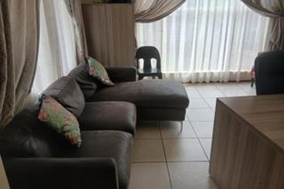 A living room area featuring tiled flooring and large windows with curtains.
