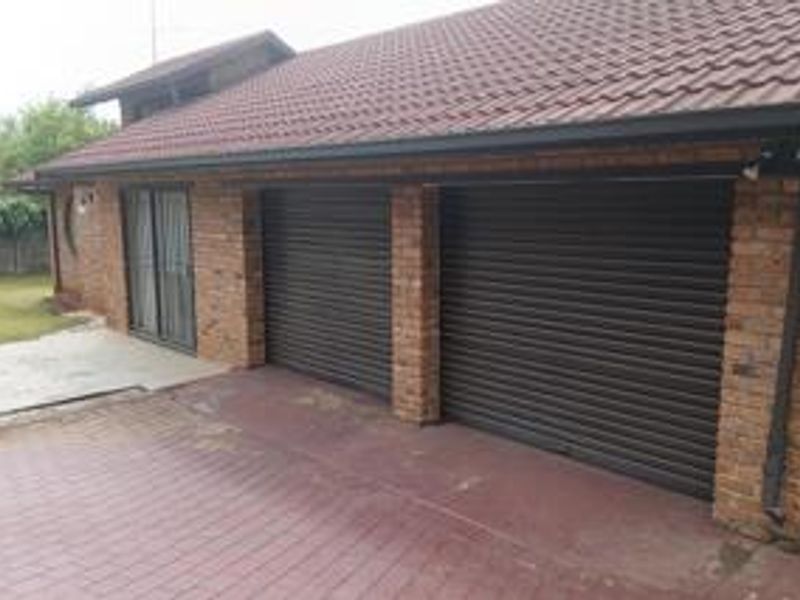 A double garage with roller doors and face brick exterior, featuring a paved driveway and adjacent sliding door access.