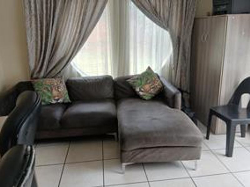 A living room area featuring tiled flooring and a large window with curtains, providing natural light to the space.