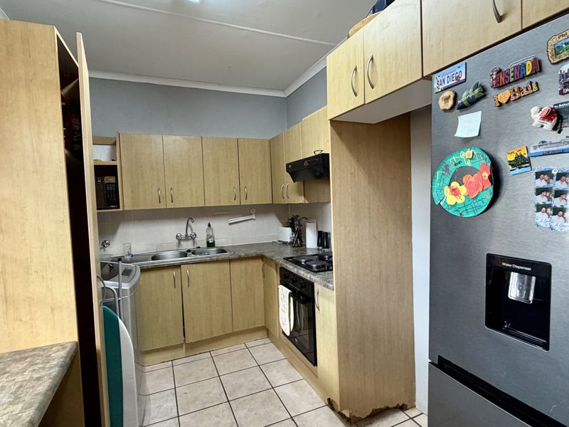 A functional kitchen featuring laminate cabinetry, a built-in oven with hob, and a double sink, showing signs of wear on the lower cabinet base.