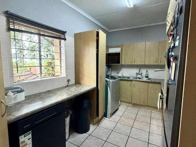 Functional kitchen featuring laminate cabinetry, ample counter space, double basin sink, and tiled flooring with a window providing natural light.