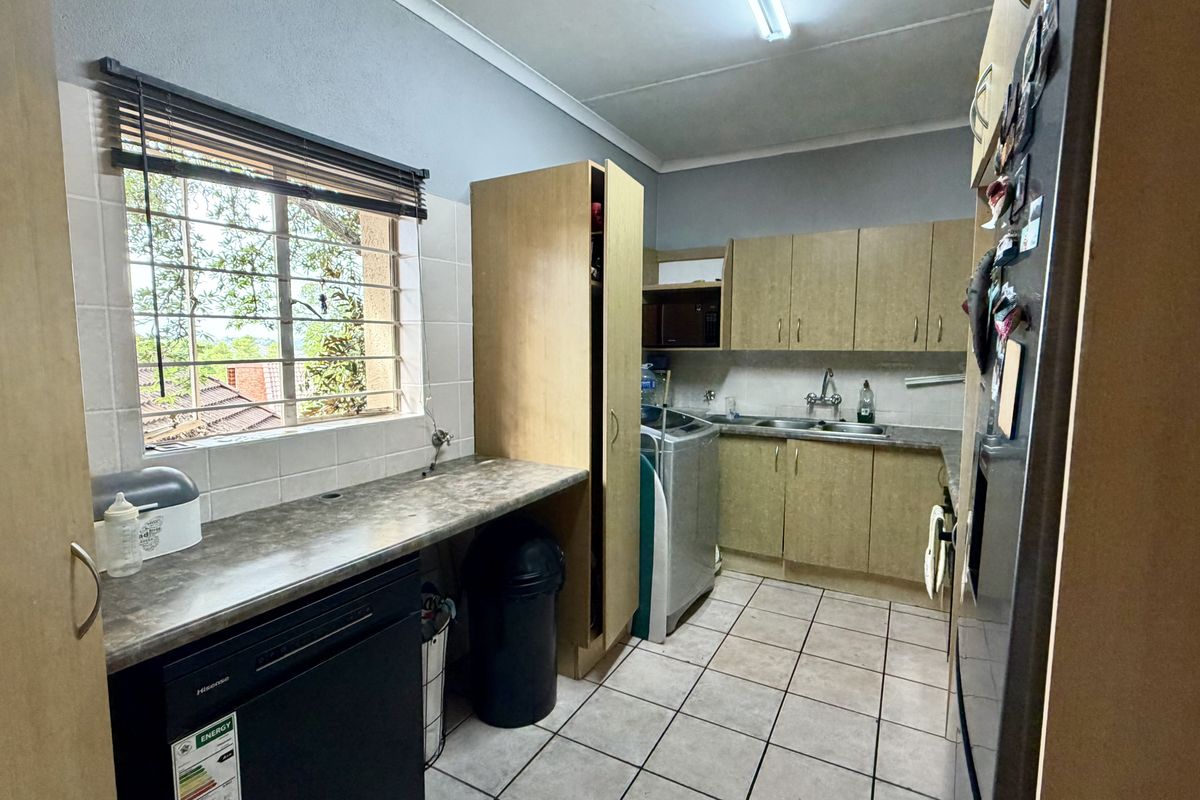Functional kitchen featuring laminate cabinetry, ample counter space, double basin sink, and tiled flooring with a window providing natural light.