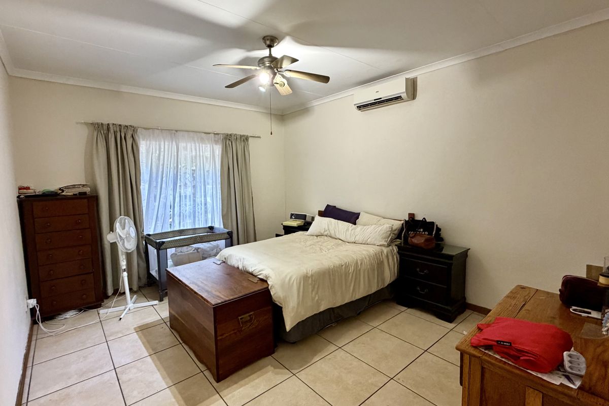A spacious bedroom featuring tiled flooring, a ceiling fan, and a wall-mounted split-system air conditioner for climate control.