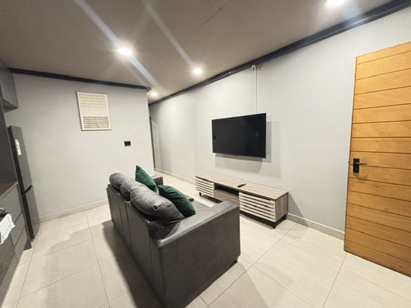 An open-plan living area featuring tiled flooring, recessed downlighting, and a modern timber door, creating a functional and contemporary space.