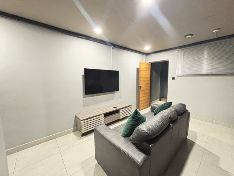 A living room featuring tiled flooring, recessed downlighting, and venetian blinds, with a neutral wall finish and a timber door leading to an adjacent space.