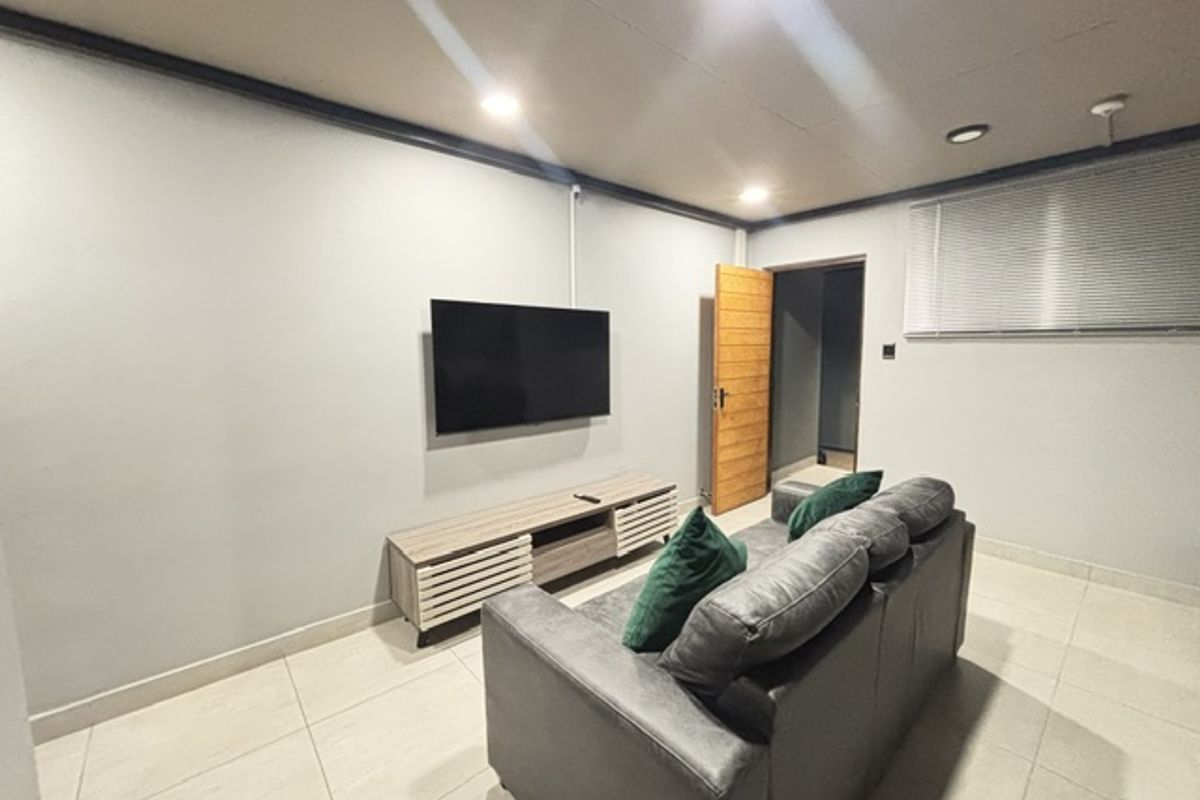 A living room featuring tiled flooring, recessed downlighting, and venetian blinds, with a neutral wall finish and a timber door leading to an adjacent space.