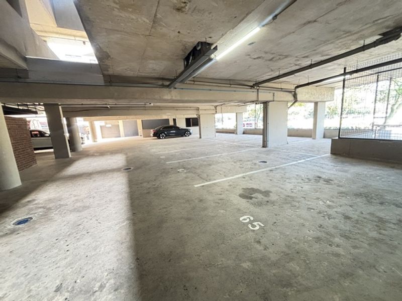 A spacious, covered concrete parking garage featuring marked parking bays, structural pillars, and overhead fluorescent lighting.