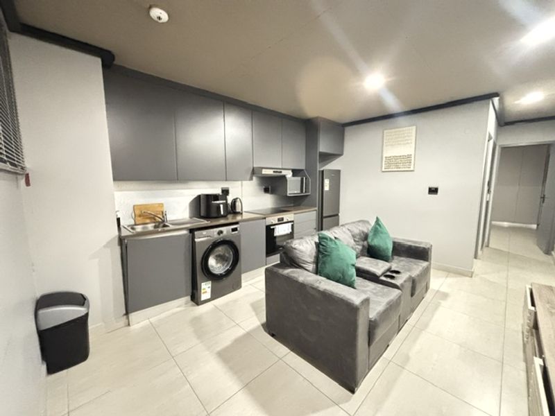 Modern open-plan living area featuring a compact kitchen with built-in cabinetry, integrated oven, extractor fan, and tiled flooring throughout.