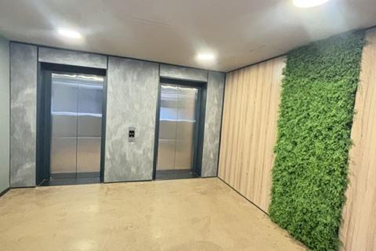 Modern apartment building lobby featuring dual elevators, polished concrete flooring, and a decorative vertical garden wall.