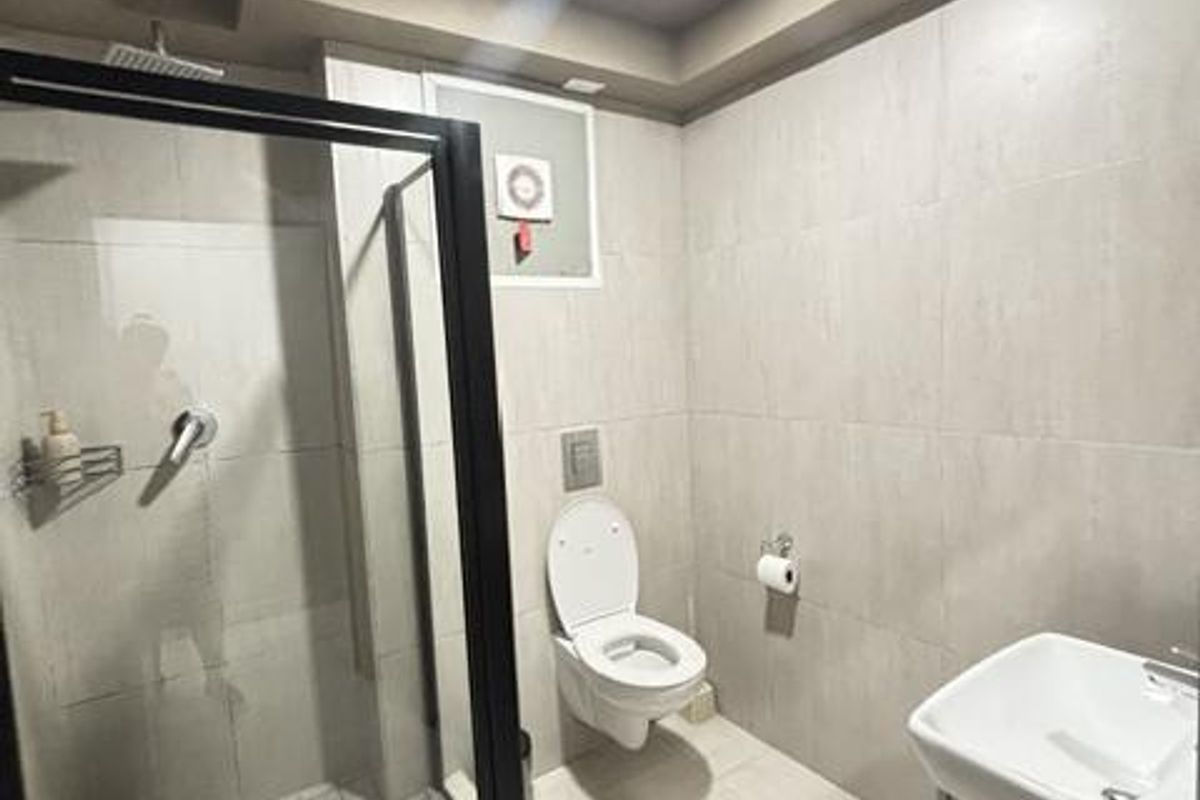 Modern bathroom featuring a walk-in shower with black-framed glass enclosure, wall-mounted toilet, and a vanity basin with neutral floor-to-ceiling tiling.