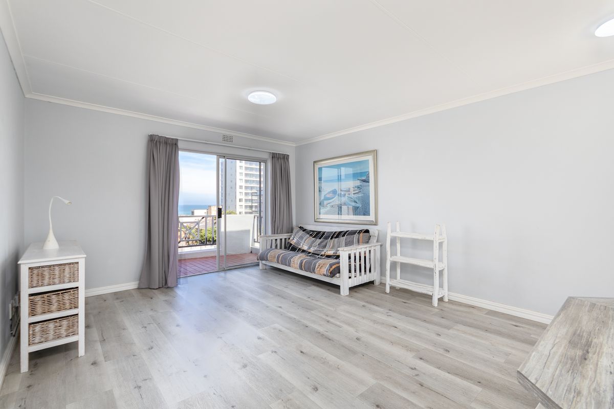 Bright living room featuring modern laminate flooring and a sliding glass door that opens onto a balcony with coastal views.
