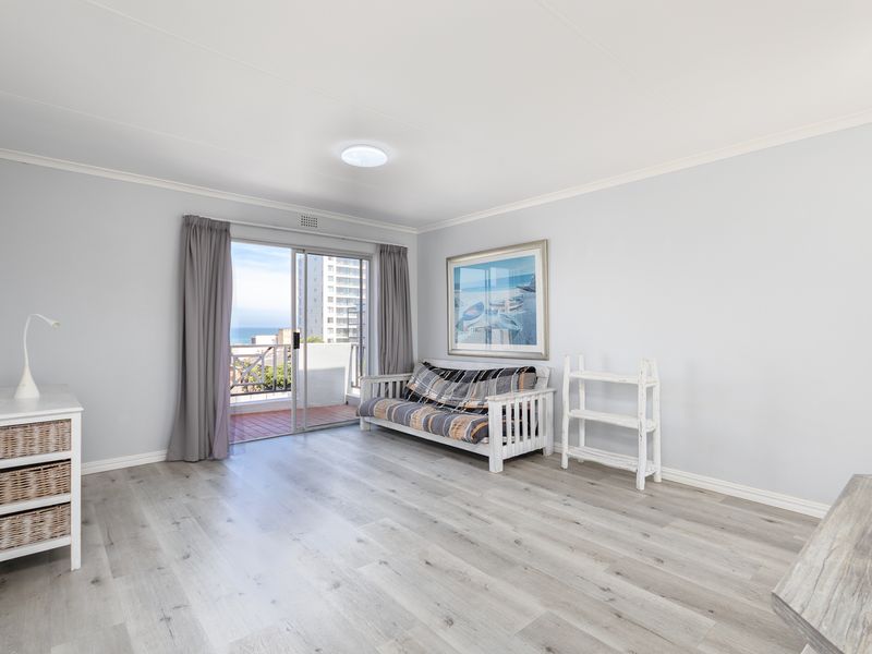 Bright living room featuring modern laminate flooring and a sliding glass door that opens onto a balcony with coastal views.
